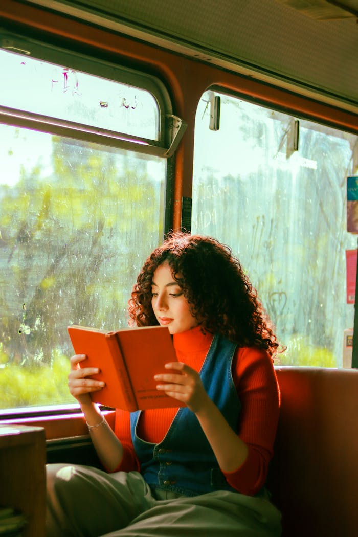 creative Young woman reading a book while traveling on a bus, bathed in natural light.